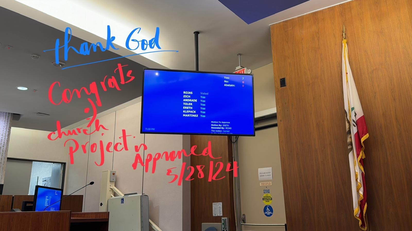 The voting screen in the Costa Mesa council chambers showing 7 yes, 0 no, with handwriting over the photo that reads: thank God, congrats, church project approved 5/28/24